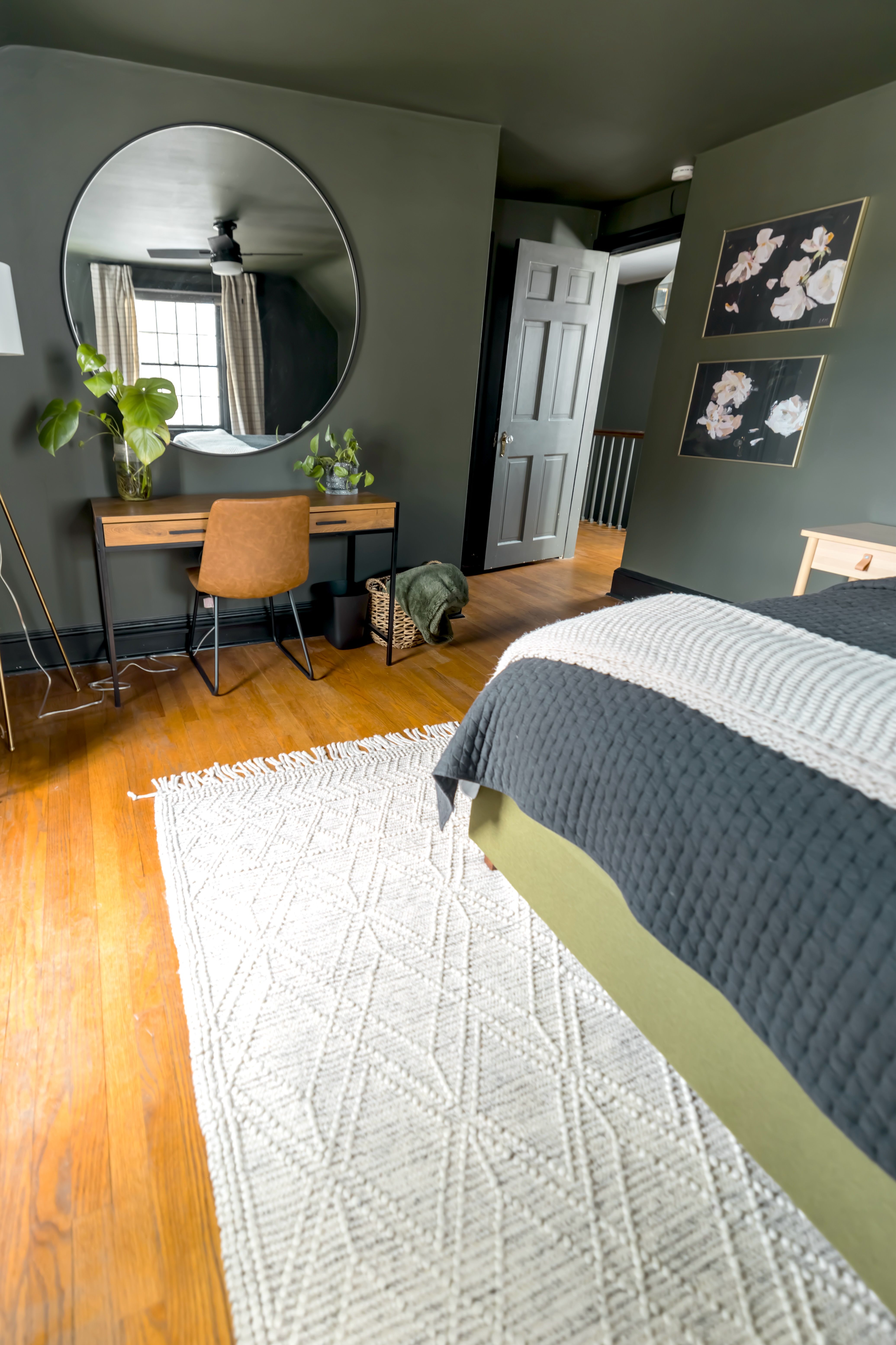 A modern bedroom with stylish decor, featuring a desk, mirror, and potted plants.
