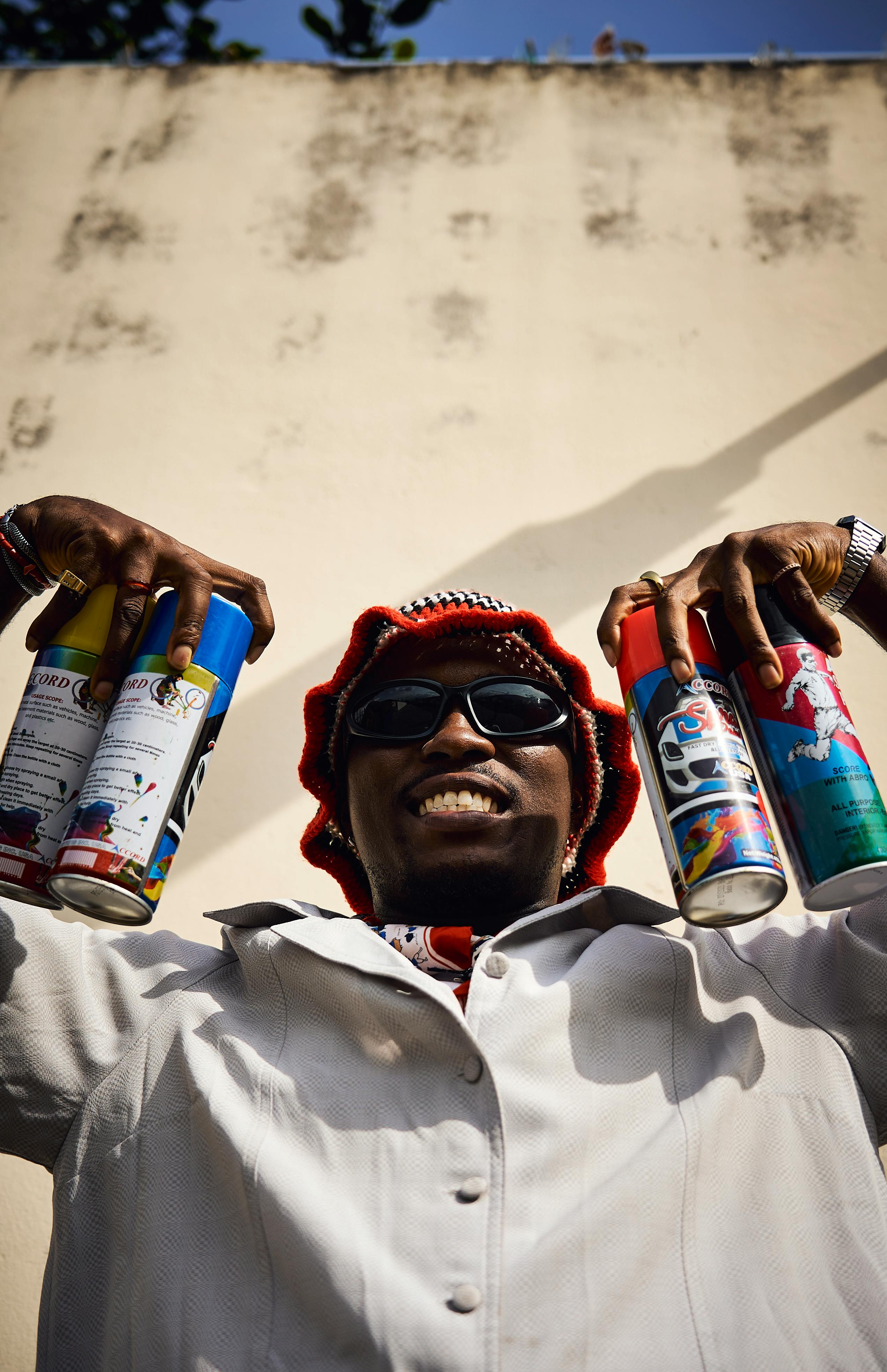 Smiling artist with spray cans ready for graffiti creation under clear sky.
