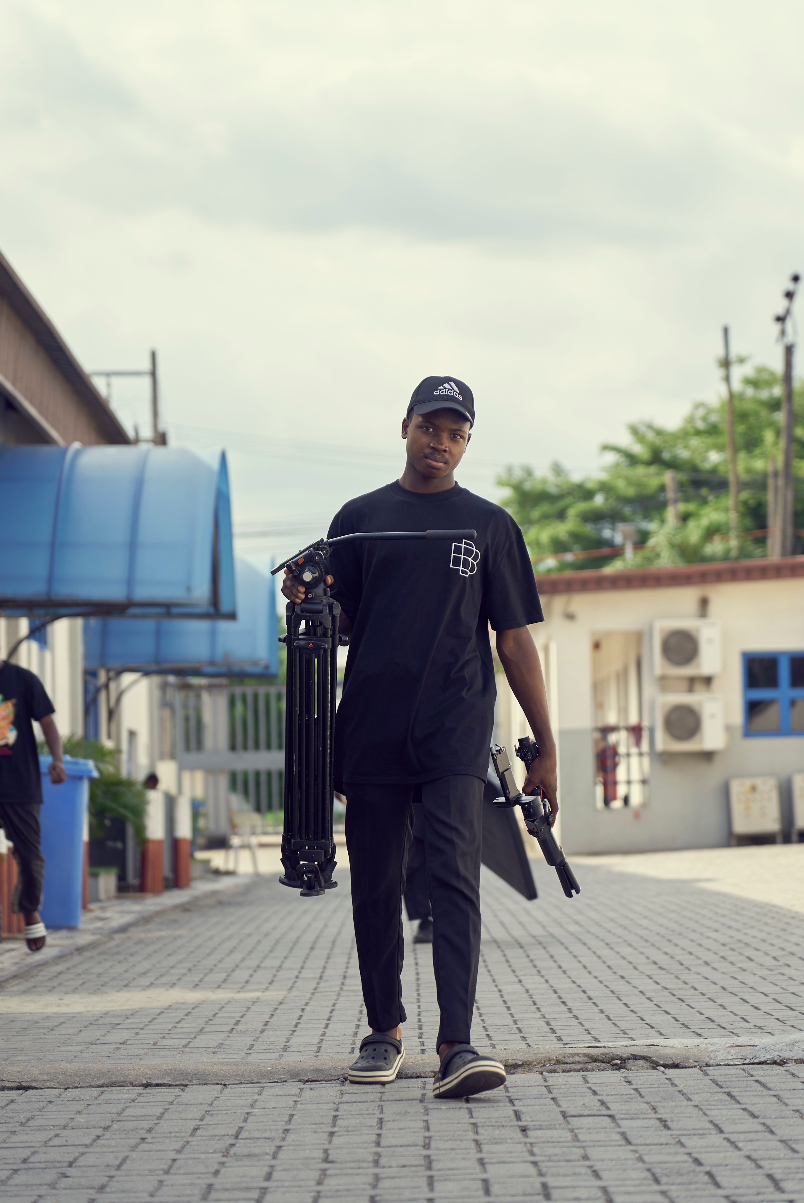 African American man carrying a tripod walking on pavement outdoors.