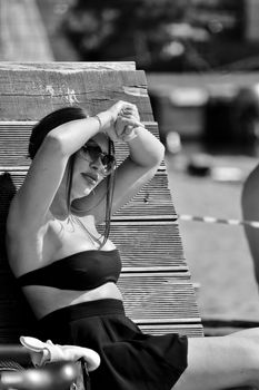 Brunette woman in black bikini top and skirt sunbathing at the beach in a monochrome scene.