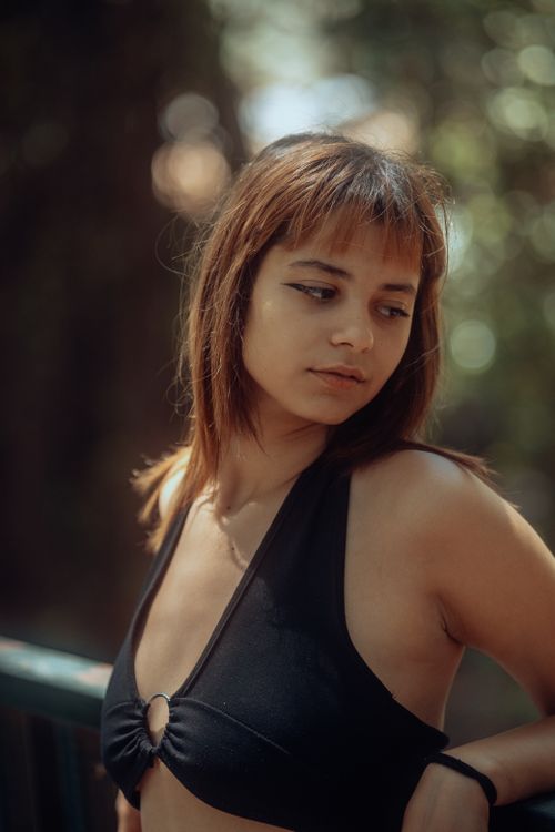 Free A young woman wearing a black bikini top poses outdoors in soft summer lighting. Stock Photo