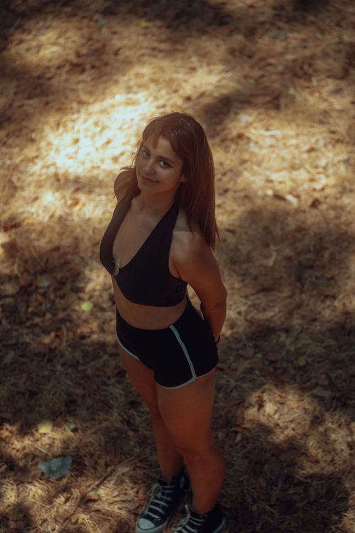 Free Brunette woman poses with a smile in a sunlit forest, wearing black sportswear. Stock Photo