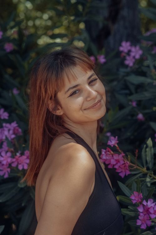 Free A happy woman in a black top smiles in a garden with pink flowers on a sunny summer day. Stock Photo