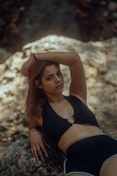 A woman in stylish black attire poses confidently against a natural rock backdrop.