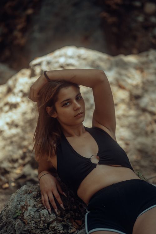 Free A woman in stylish black attire poses confidently against a natural rock backdrop. Stock Photo