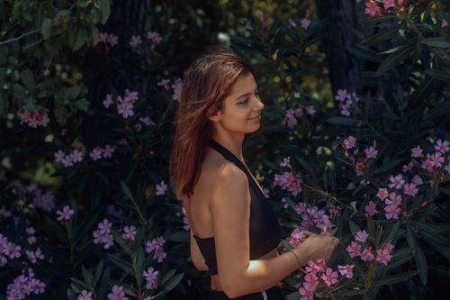 Free A woman in a black top smiles beside pink flowers in a garden. Stock Photo