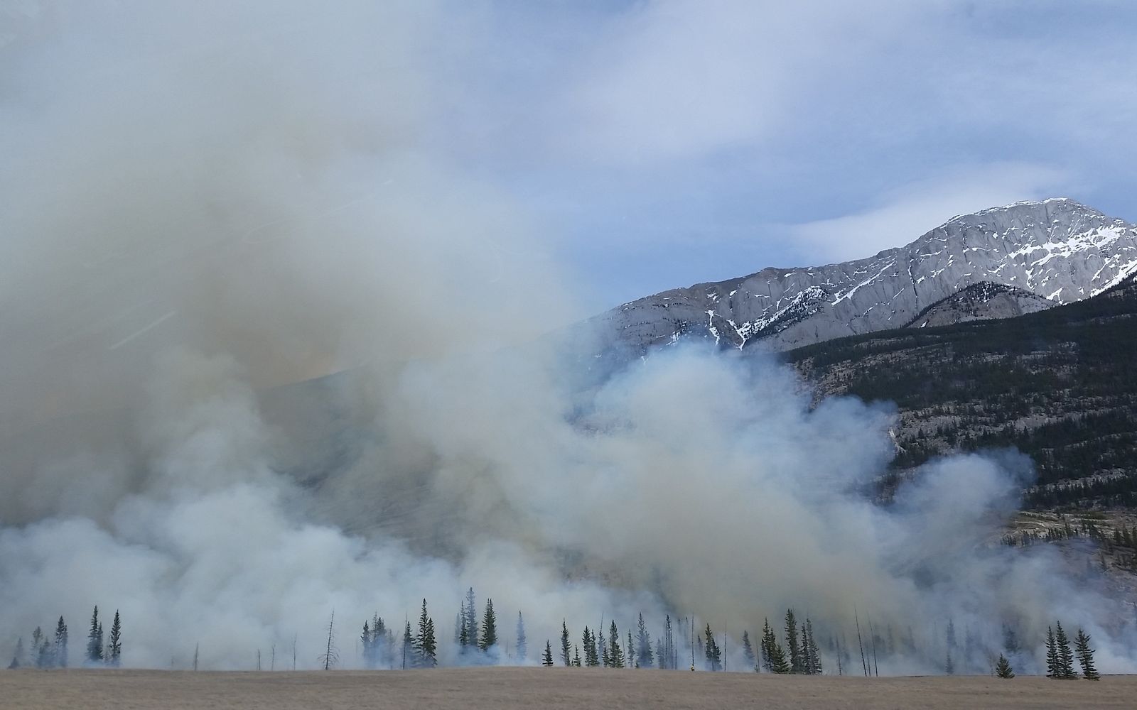 Thick wildfire smoke billowing over a forested mountain landscape