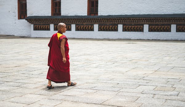 A Buddhist monk in traditional attire walks through a courtyard in Bhutan, showcasing spiritual tranquility.