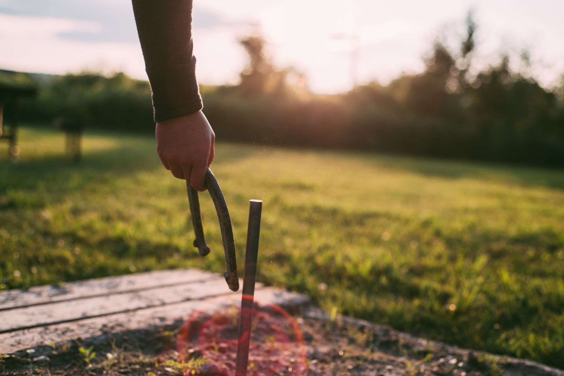Photo of Person's Hand Holding a Horseshoe Next to Metal Stake in the Ground