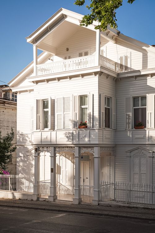 Free Charming white Victorian house facade illuminated by warm sunlight on a serene street. Stock Photo
