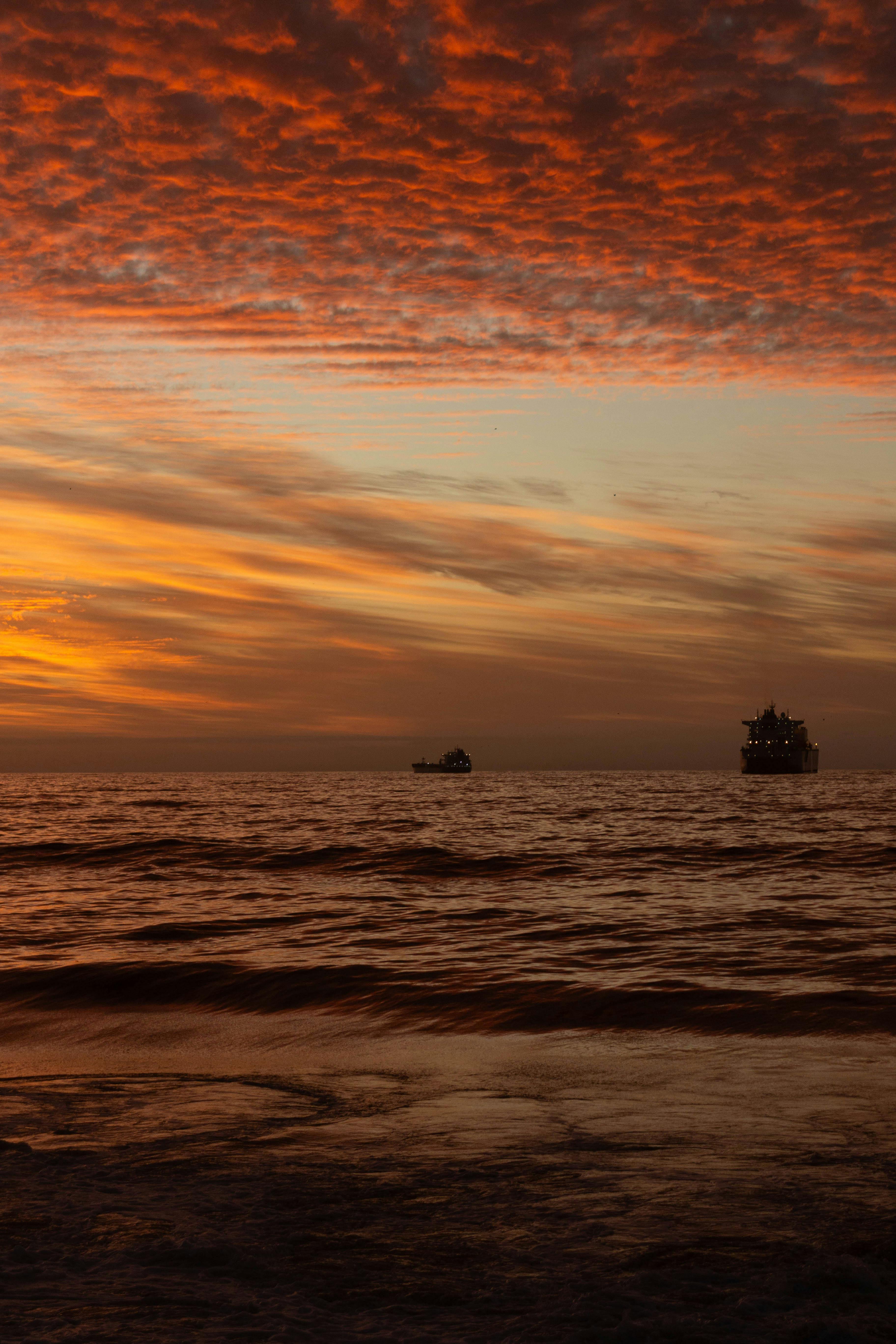 A dramatic sky at sunset over the sea with silhouettes of ships on the horizon.