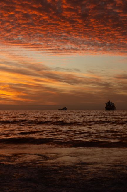 A dramatic sky at sunset over the sea with silhouettes of ships on the horizon.