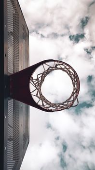 Upward view of a basketball hoop against a cloudy sky, featuring net and backboard.