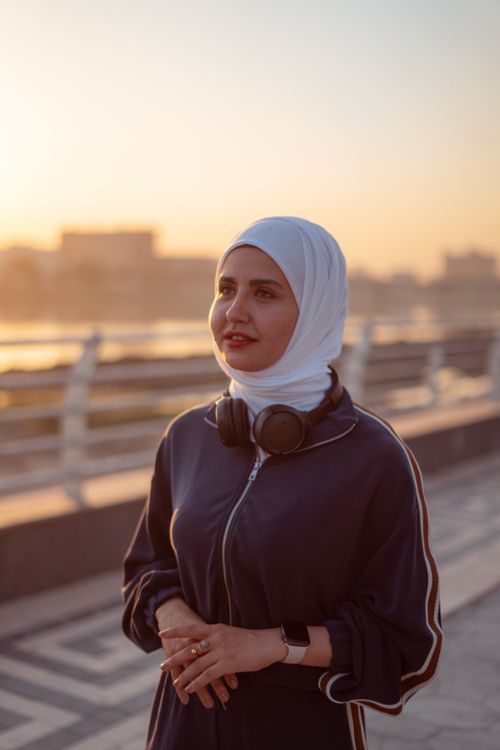 Free Portrait of a Muslim woman wearing a hijab and headphones, standing outdoors in Baghdad during sunset. Stock Photo