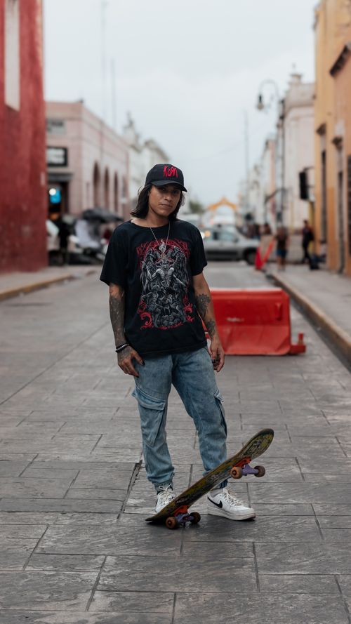Free A young skateboarder poses on an urban street with colorful buildings. Stock Photo