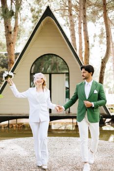 A fashionable wedding couple poses in front of a modern A-frame house in Istanbul, Türkiye, expressing joy and love.