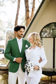 Bride and groom pose in stylish attire amidst İstanbul's serene garden setting.