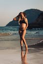 日落时分，一位穿着比基尼的准妈妈戴着遮阳帽，在海滩海岸线上摆姿势