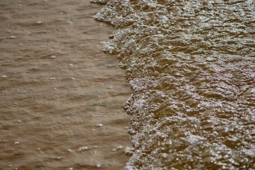 Close-up view of small waves rolling onto a sandy beach, capturing texture and movement.