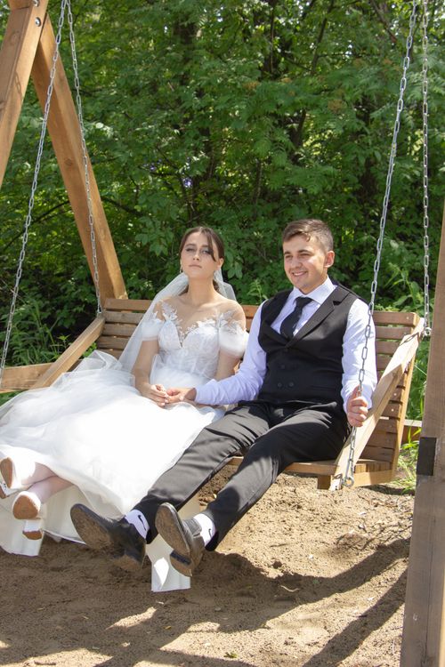 Free A newlywed bride and groom relax on a wooden swing outdoors on a sunny summer day. Stock Photo