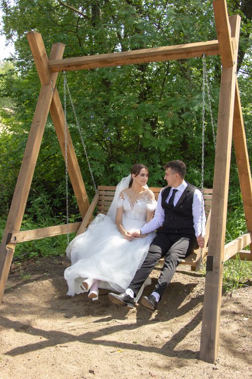 Free A loving couple in wedding attire sharing a moment on a rustic swing in a serene park. Stock Photo