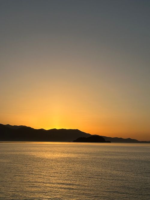 Free Beautiful sunset over the Aegean Sea in Türkiye with calm waters and silhouetted mountains. Stock Photo