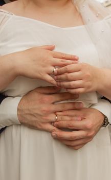 Intimate hands-on wedding moment with newlyweds' rings and embrace.