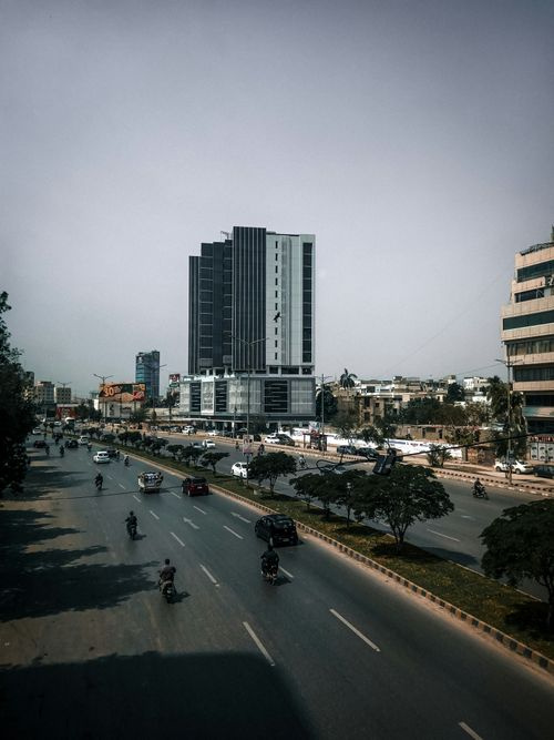 Free A bustling urban street featuring a tall modern building and light traffic in daylight. Stock Photo