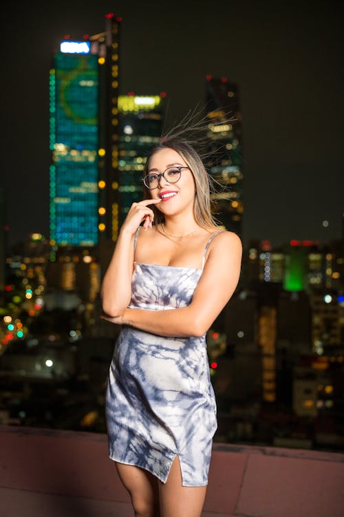 A woman in a dress standing on a rooftop with city lights in the background