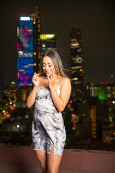 Stylish young woman in a mini dress smiling against the illuminated Mexico City skyline at night.