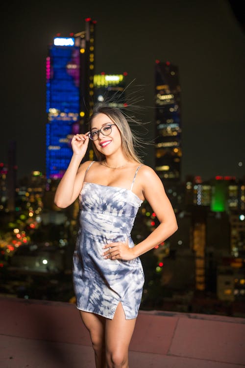 A woman in a dress standing on a rooftop with city lights in the background