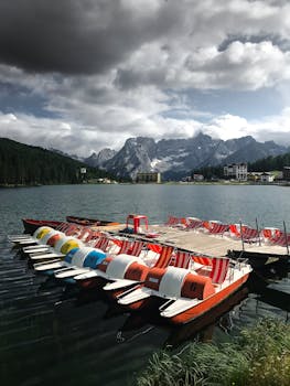 一排色彩缤纷的踏板船停靠在宁静的山间湖泊上，坐拥令人惊叹的高山景色