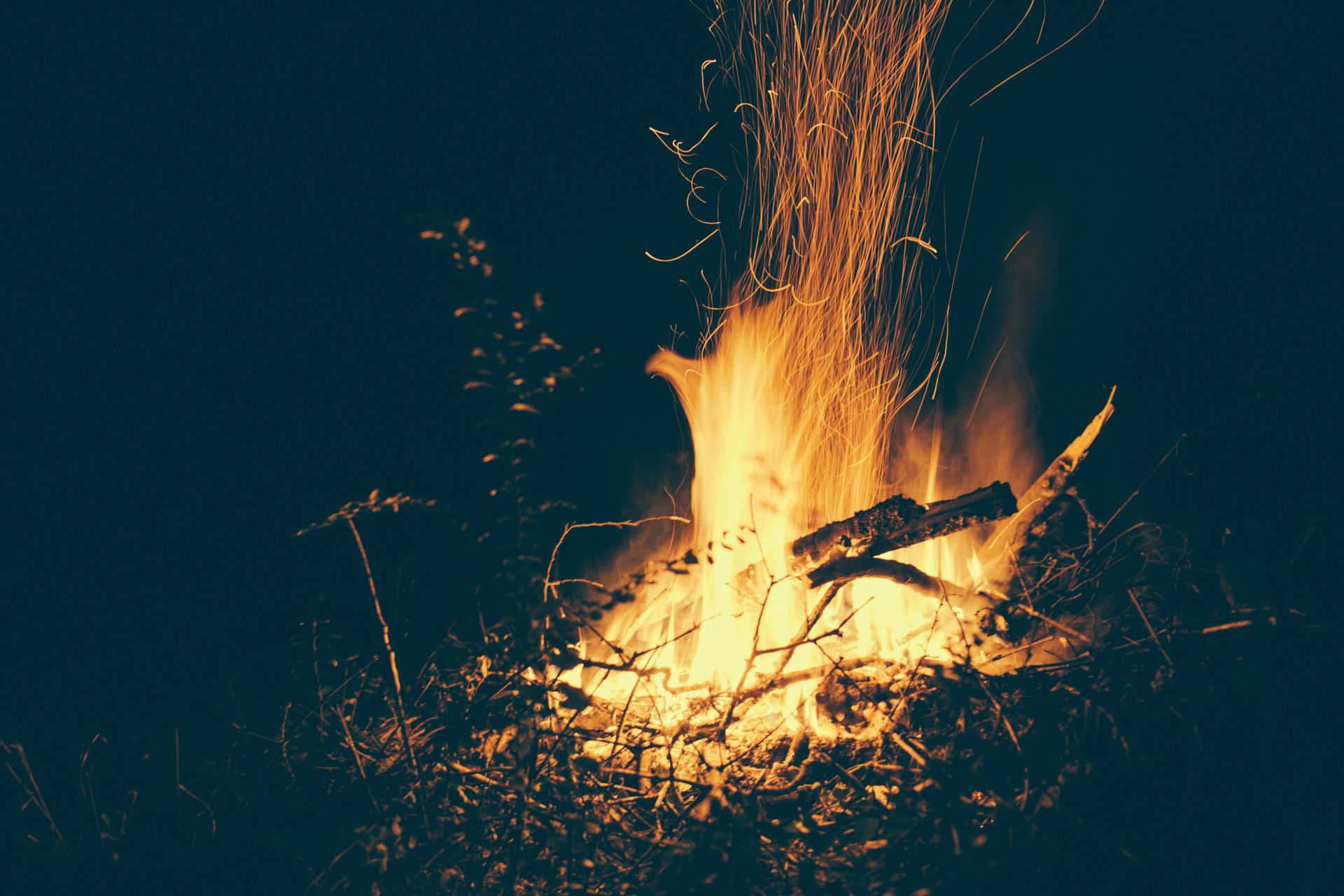 Captivating bonfire blaze captured at night, revealing intense flames and sparks in the dark outdoors.
