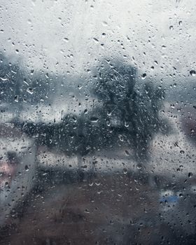 Raindrops on a window, capturing a serene and moody rainy day with a blurred outdoor view.