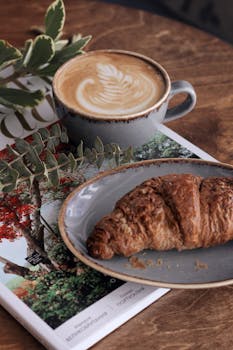 清晨景色迷人，木桌上摆着拿铁咖啡和羊角面包，非常适合享用一顿舒适的早餐