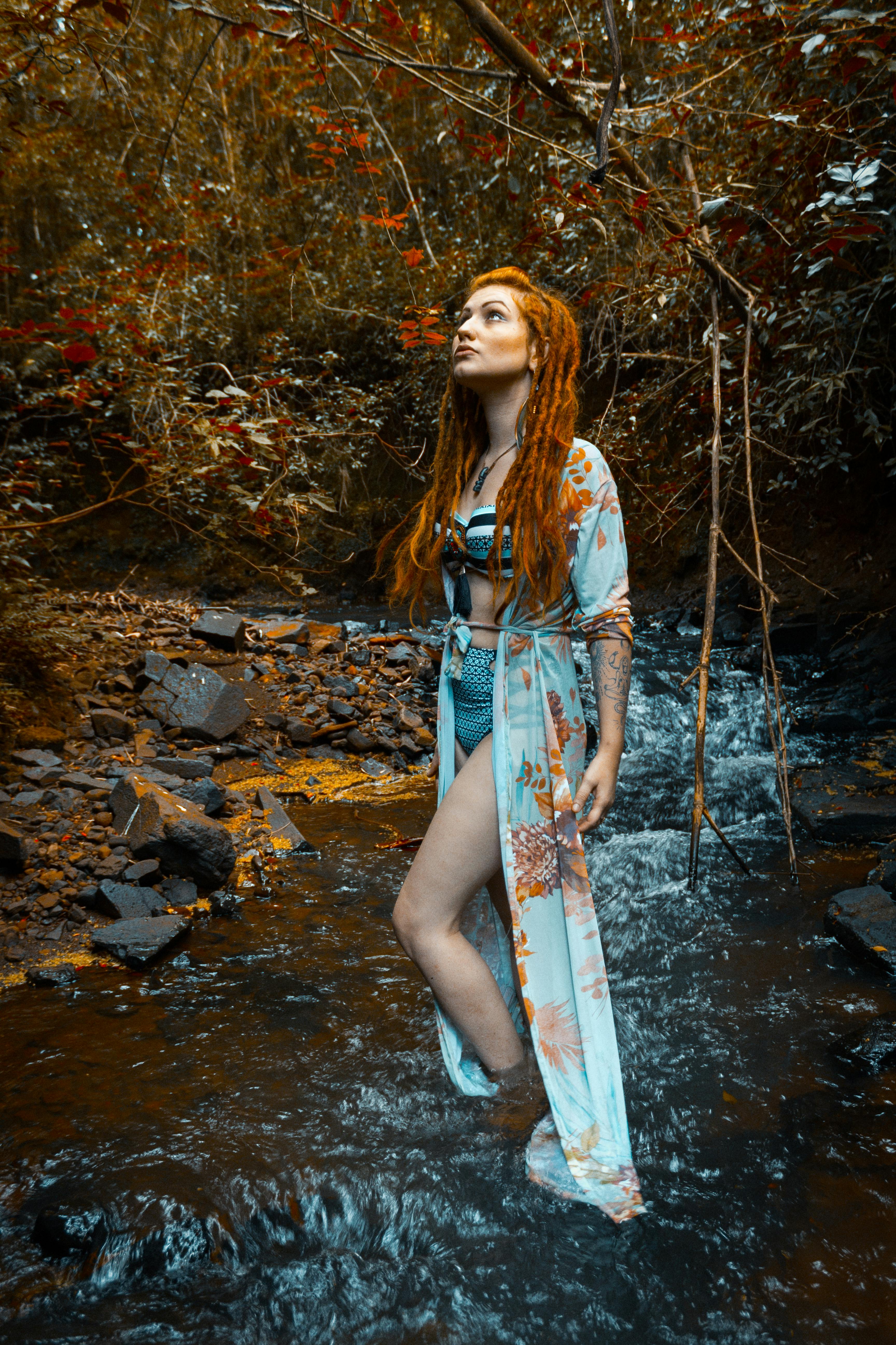 秋日的森林里，一名女子身着飘逸的连衣裙，在小溪边摆着姿势