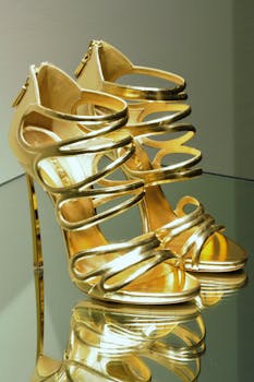 Striking golden high-heeled shoes elegantly displayed on a reflective glass surface.