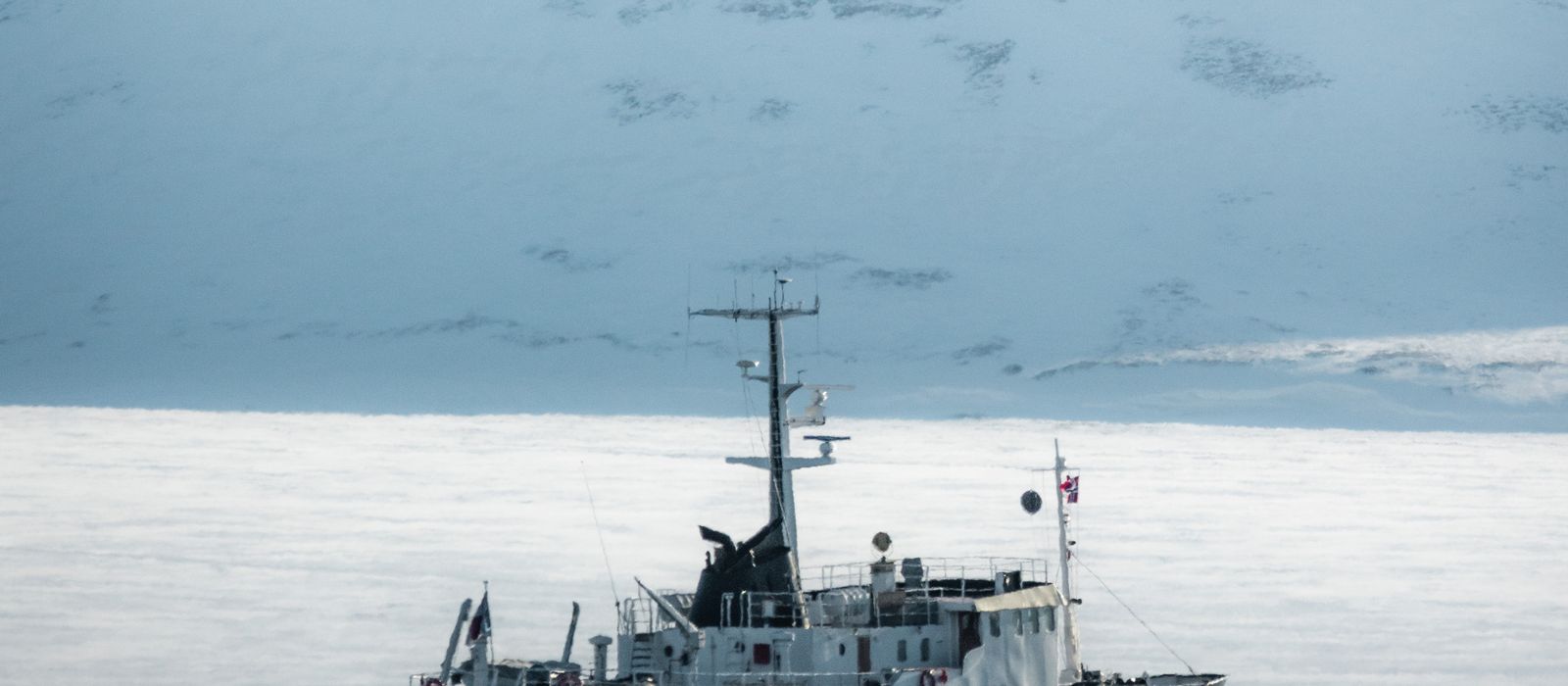 An expedition ship moving through a foggy Arctic fjord ringed by snow-covered mountains.