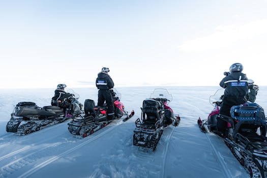A group of tourists on snowmobiles explore the vast Arctic landscape under clear skies.