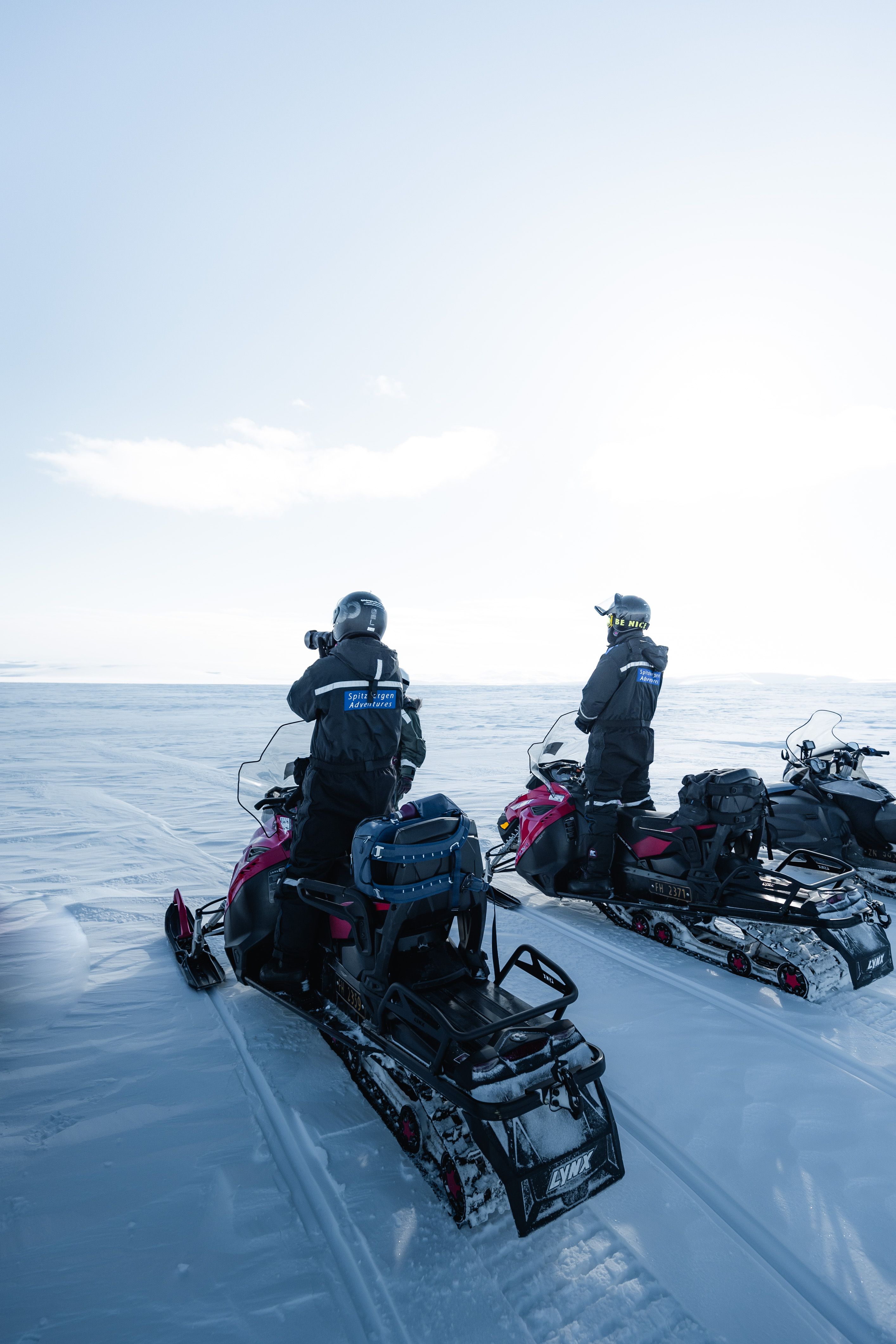 Two snowmobilers exploring vast icy landscape under bright daylight.
