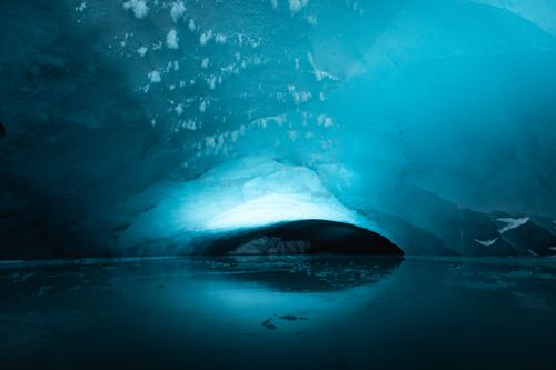 Free Majestic view inside an ice cave with a captivating blue glow and reflections on icy water. Stock Photo