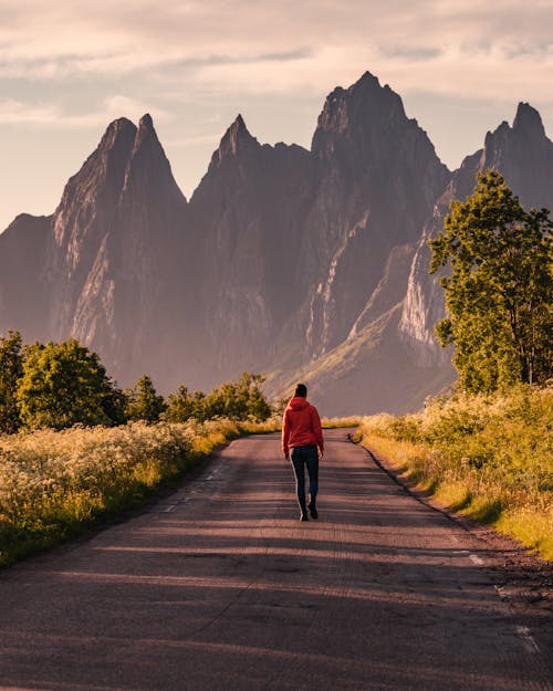 Человек в красной толстовке идет по дороге к горам