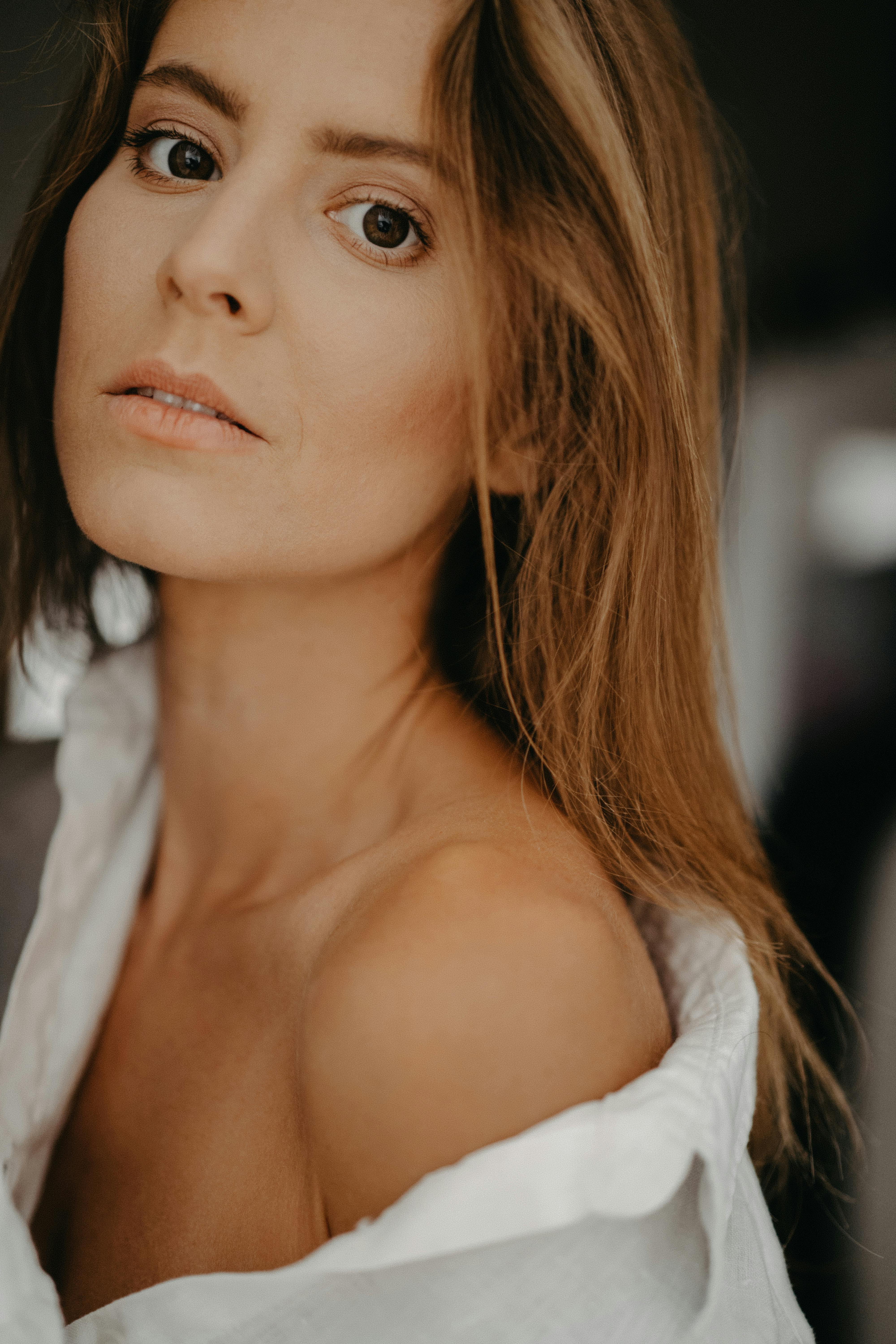 A close-up portrait of a brunette woman in a white shirt with a neutral background.