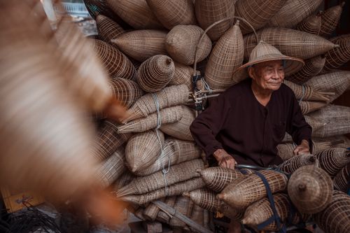 Free An elderly man sits among handmade fishing baskets at an outdoor market display. Stock Photo