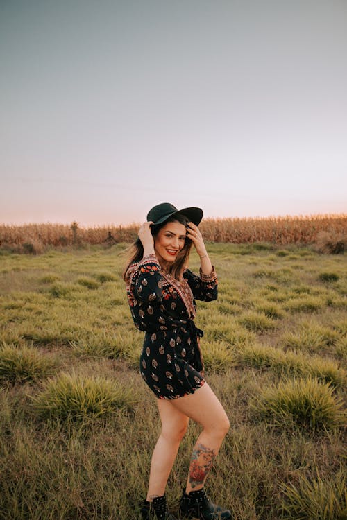 Photo of Woman Holding Her Hat While Standing on Grass Field