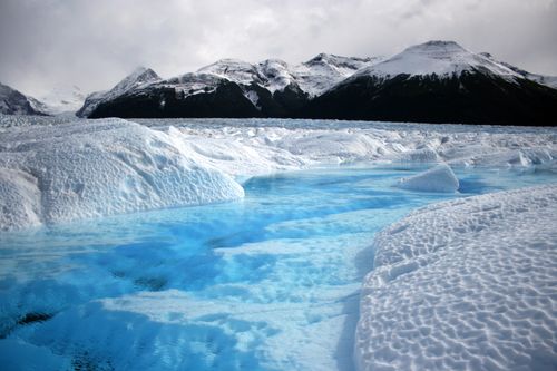 Free A breathtaking view of a blue frozen river flowing through a snow-covered glacier landscape. Stock Photo