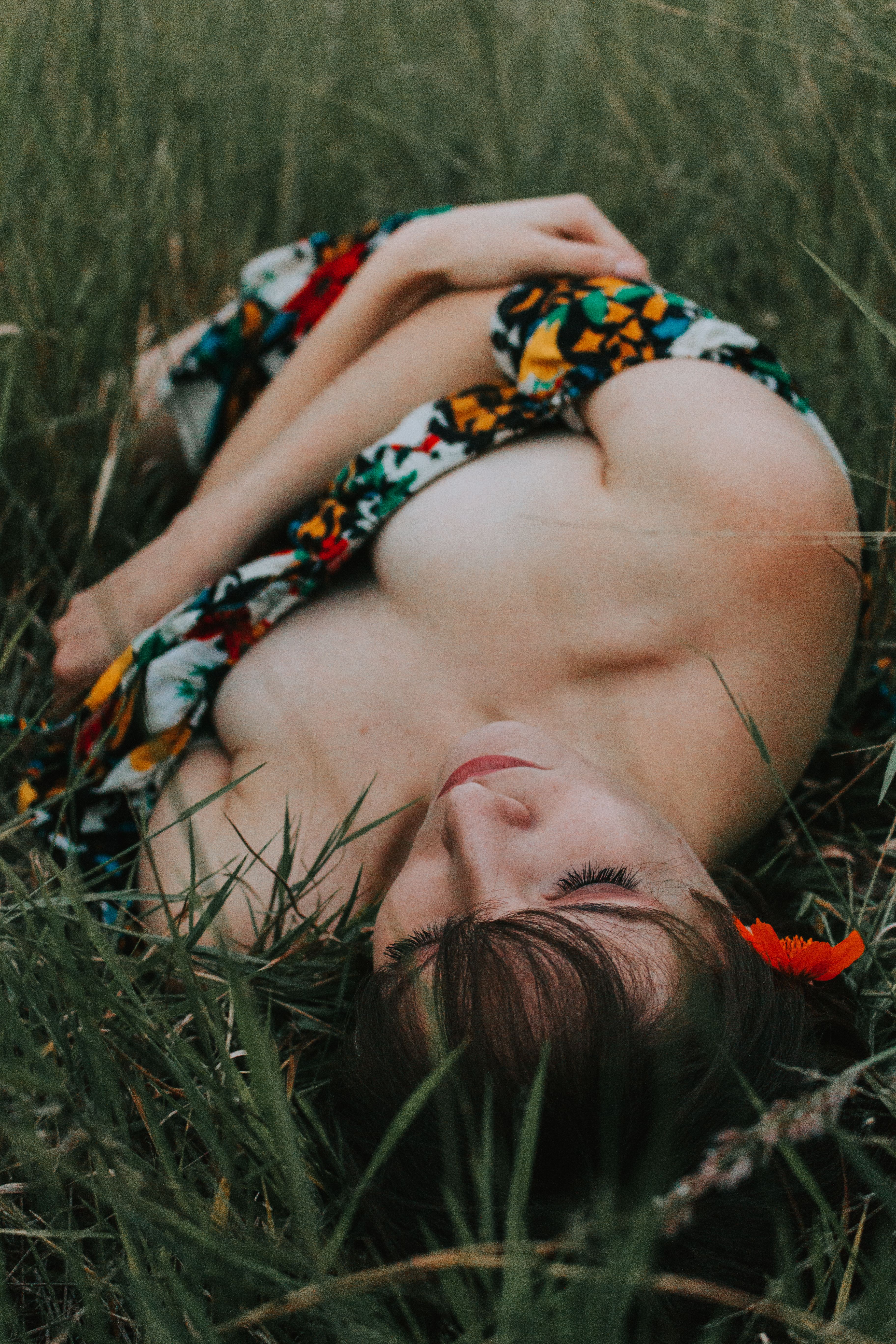 A woman in a colorful dress lies peacefully in a lush green field, creating a serene portrait.