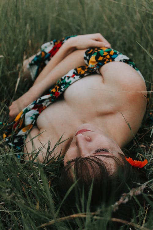 A Woman in a Colorful Dress Lying on a Green Grass Field 