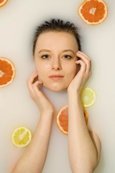 Relaxing portrait of a woman in a milk bath with citrus slices, embodying freshness and self-care.