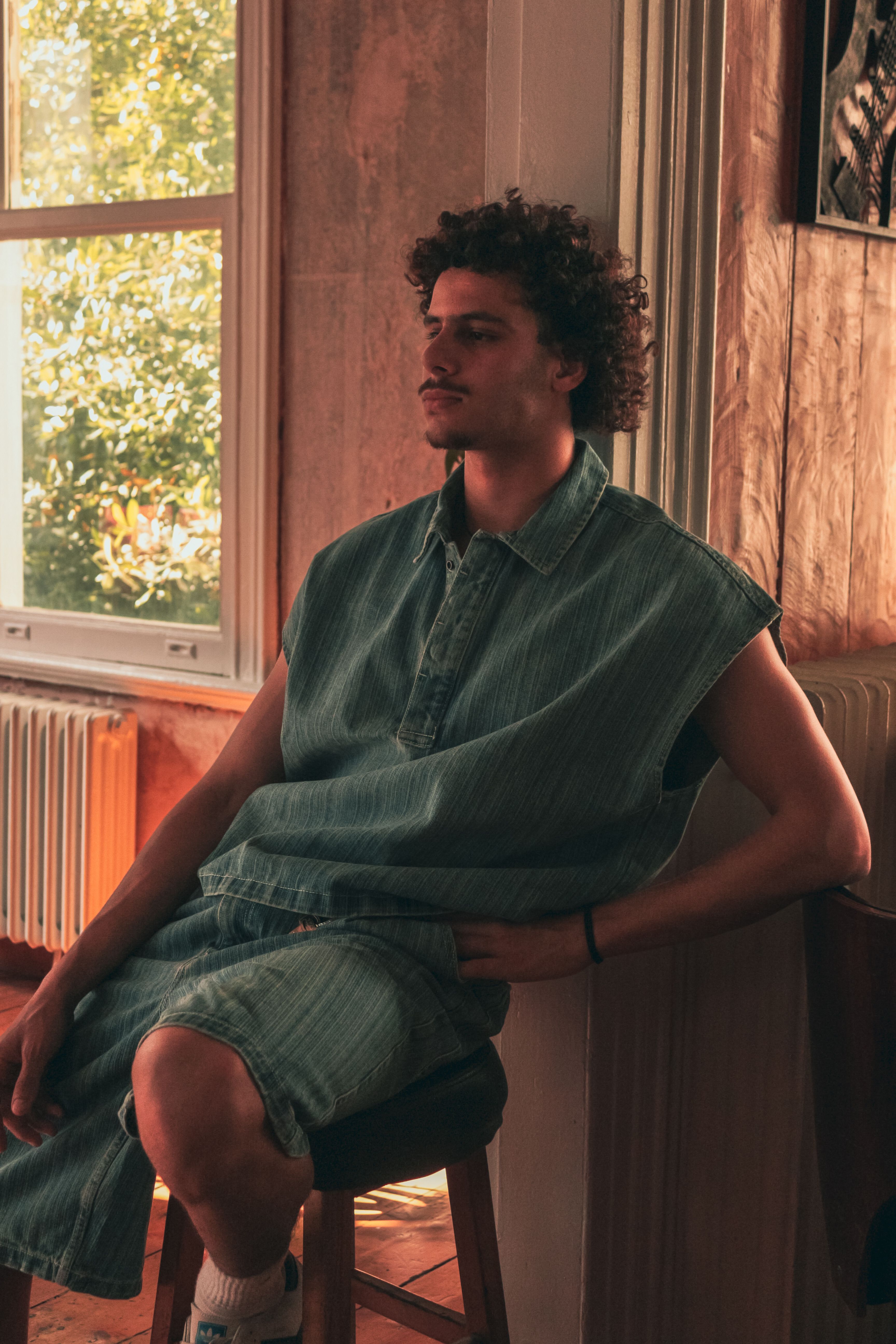 Young male model in denim attire sitting confidently in a bright room.